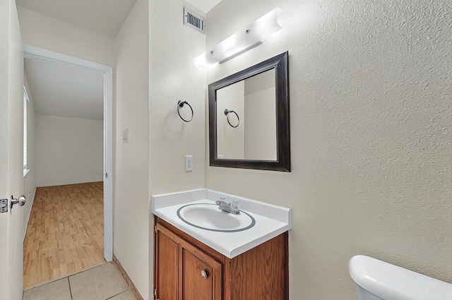 half bathroom with toilet, tile patterned floors, visible vents, and vanity
