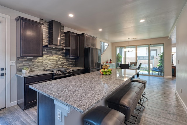 7754 Majesty Ct NW, Albuquerque, NM 87107 - kitchen featuring wall chimney exhaust hood, freestanding refrigerator, gas range, a breakfast bar, and recessed lighting
