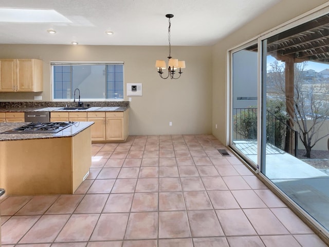 kitchen with light brown cabinetry, a chandelier, stainless steel gas cooktop, light tile patterned flooring, and a sink