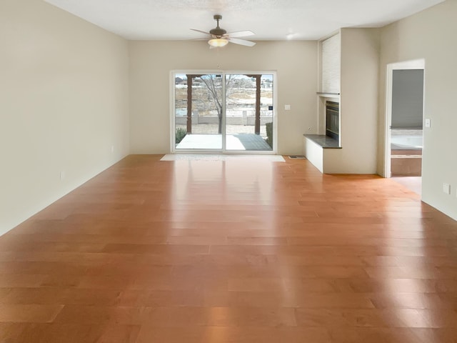 unfurnished living room with a large fireplace, light wood-type flooring, and ceiling fan