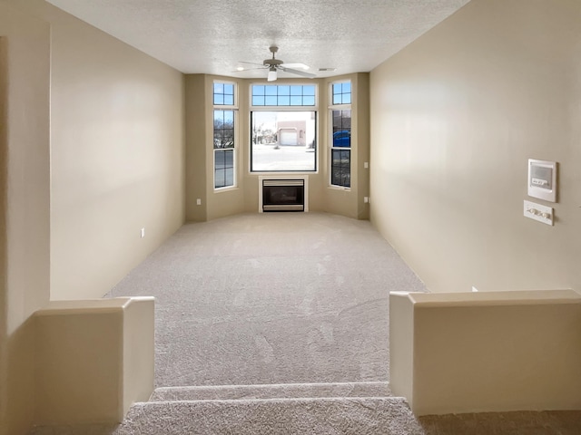 unfurnished living room featuring carpet floors, a textured ceiling, and ceiling fan