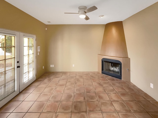 unfurnished living room with light tile patterned floors, french doors, a large fireplace, and a ceiling fan