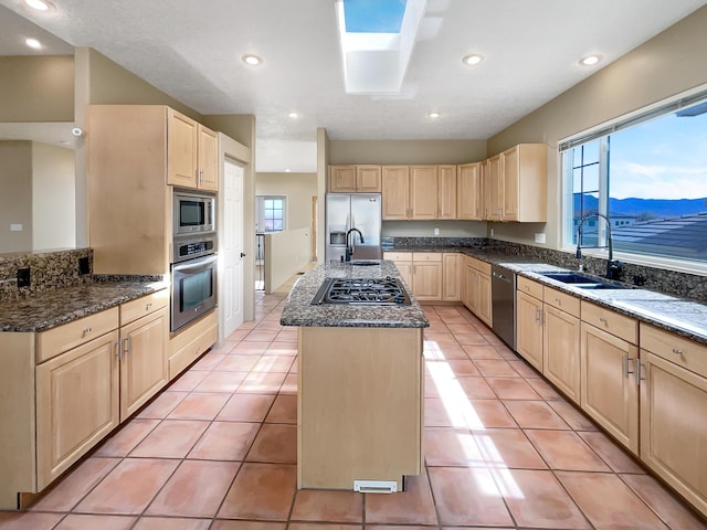 kitchen with dark stone countertops, an island with sink, light brown cabinets, and appliances with stainless steel finishes