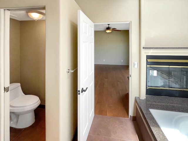 bathroom with vanity, a ceiling fan, a glass covered fireplace, tile patterned floors, and toilet