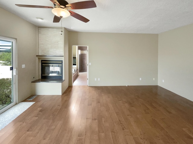 unfurnished living room featuring a ceiling fan, visible vents, wood finished floors, a multi sided fireplace, and a textured ceiling