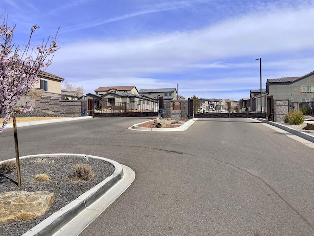 12136 Bear Valley Ln NW, Albuquerque, NM 87120 - view of asphalt road with a gate, curbs, a residential view, a gated entry, and street lighting