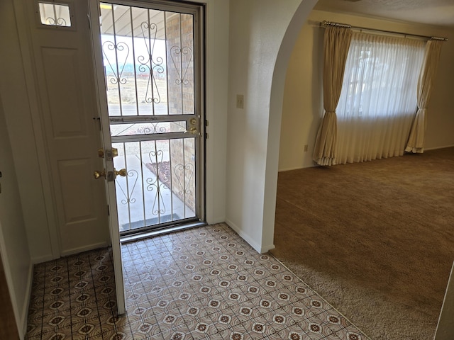 foyer entrance with baseboards, arched walkways, and light carpet