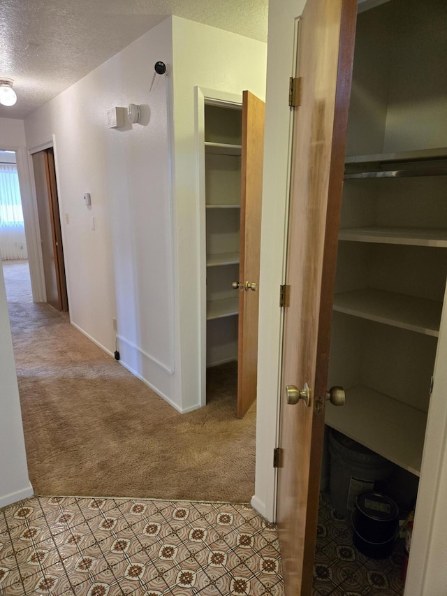 corridor with carpet, baseboards, and a textured ceiling