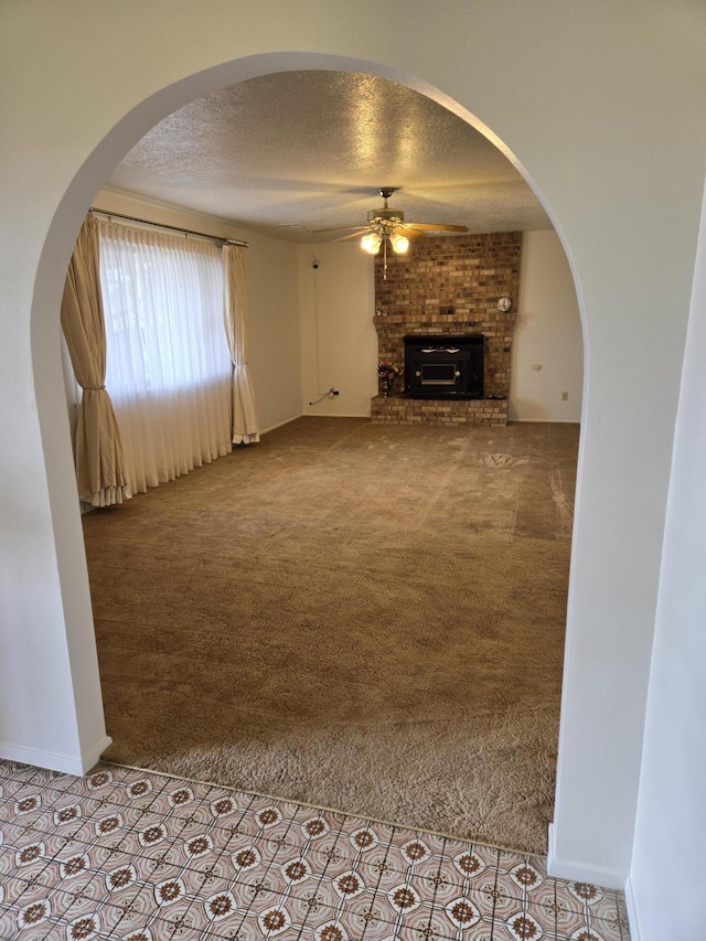 unfurnished living room featuring baseboards, carpet, a fireplace, a textured ceiling, and a ceiling fan