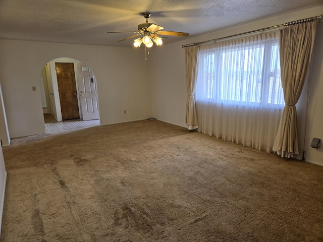 unfurnished room with a ceiling fan, carpet, arched walkways, and a textured ceiling