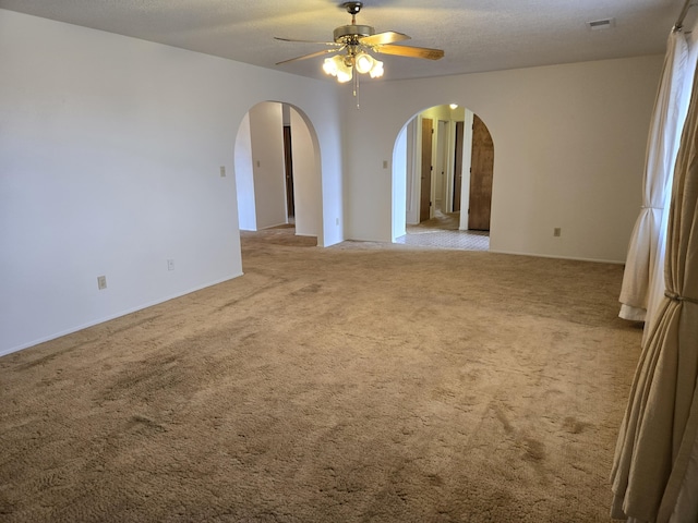 unfurnished room featuring visible vents, light colored carpet, arched walkways, a textured ceiling, and a ceiling fan