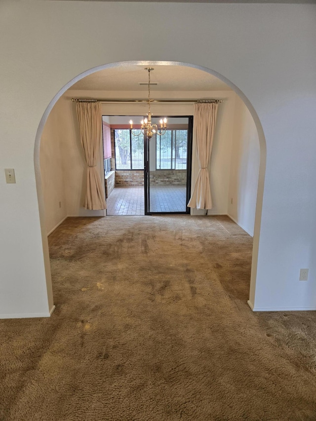 carpeted empty room with baseboards, arched walkways, and a chandelier