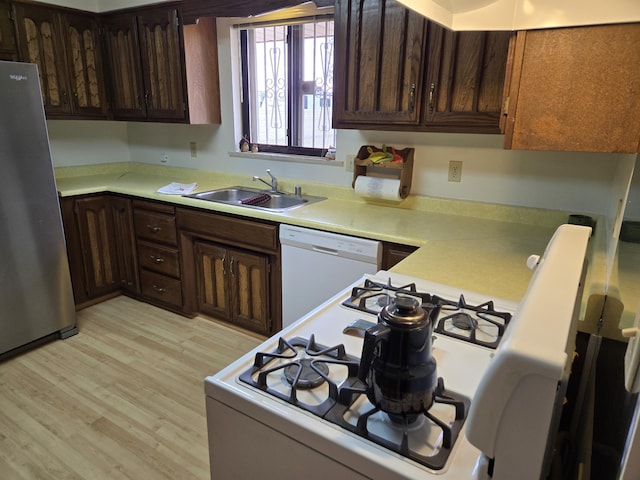 kitchen with white appliances, a sink, light countertops, dark brown cabinets, and light wood-style floors