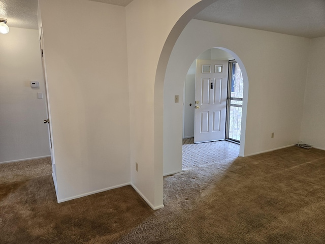 carpeted entrance foyer with baseboards, arched walkways, and a textured ceiling