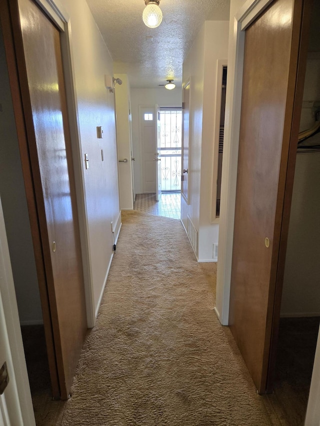 hall featuring a textured ceiling, baseboards, and carpet floors