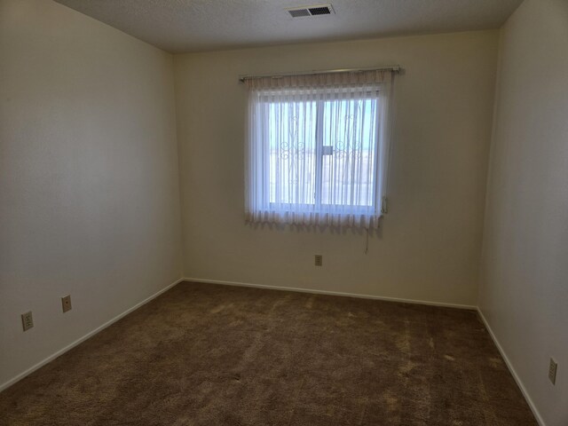 unfurnished room featuring visible vents, a textured ceiling, baseboards, and dark colored carpet