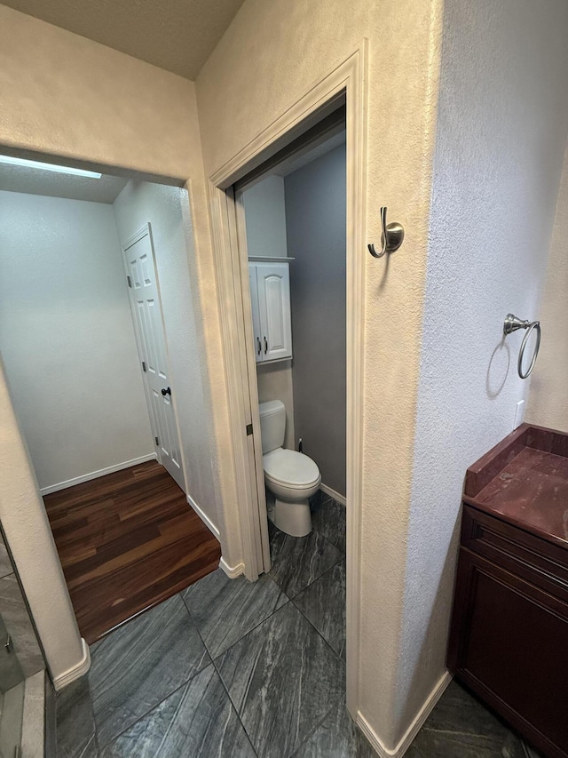 bathroom featuring baseboards, a textured wall, and toilet