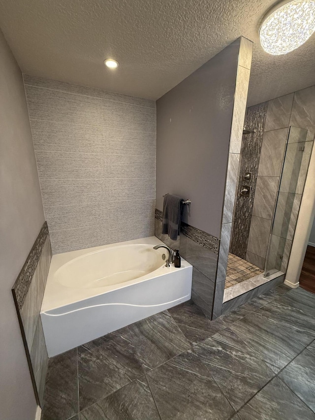 bathroom with marble finish floor, tile walls, a textured ceiling, a bath, and a shower stall