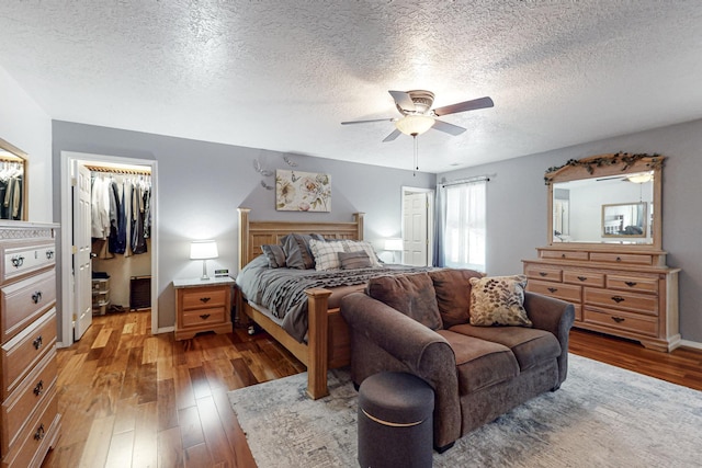 bedroom with ceiling fan, a walk in closet, light wood-style floors, a textured ceiling, and a closet