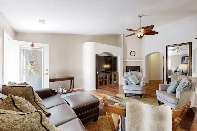 living room featuring visible vents, lofted ceiling, ceiling fan, light wood-type flooring, and arched walkways