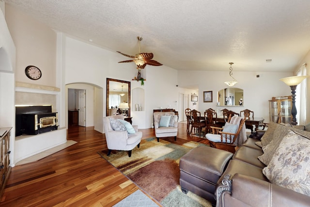 living room featuring ceiling fan, a textured ceiling, arched walkways, wood finished floors, and high vaulted ceiling