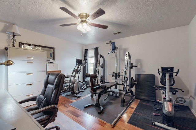 exercise area with a textured ceiling, ceiling fan, light wood-style flooring, and visible vents