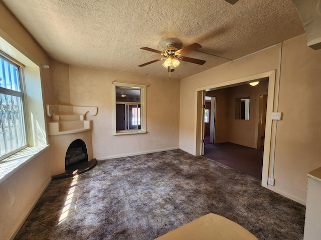 912 Camino Del Pueblo, Bernalillo, NM 87004 - unfurnished living room with baseboards, a fireplace with raised hearth, a textured ceiling, and ceiling fan