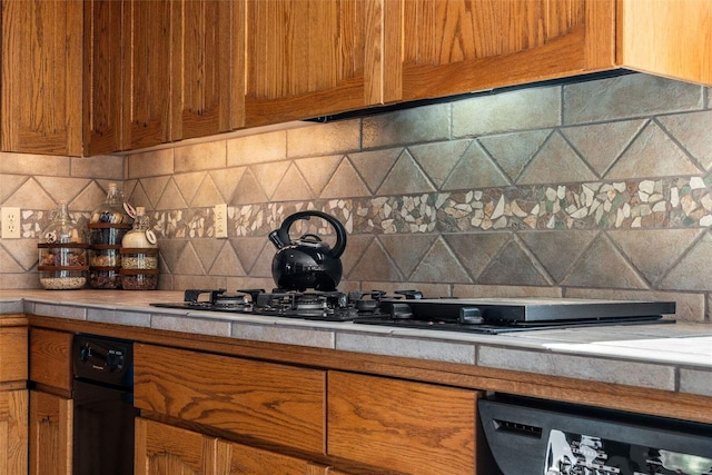 kitchen featuring brown cabinets, light countertops, black appliances, and backsplash