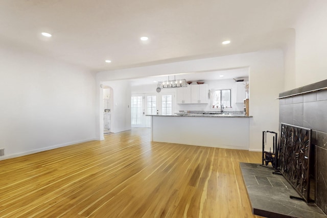 living area featuring light wood-type flooring, recessed lighting, a tiled fireplace, baseboards, and a notable chandelier