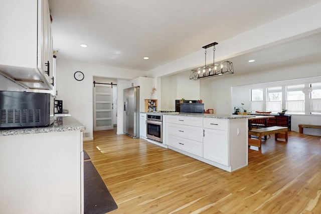 kitchen featuring white cabinets, a barn door, appliances with stainless steel finishes, recessed lighting, and light wood finished floors