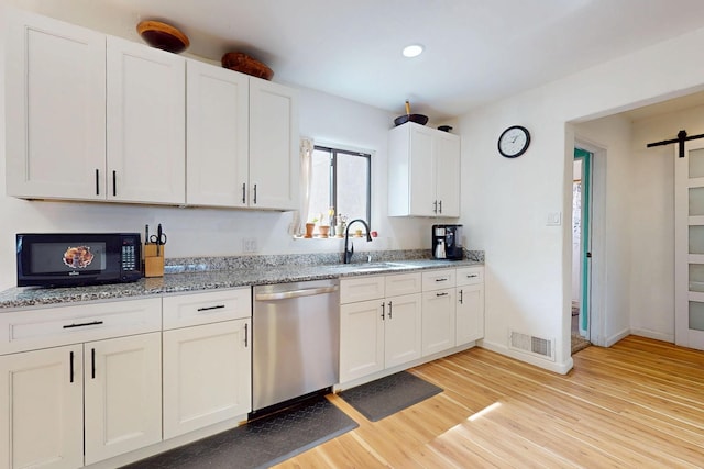 kitchen featuring visible vents, dishwasher, a sink, light stone countertops, and light wood-style flooring