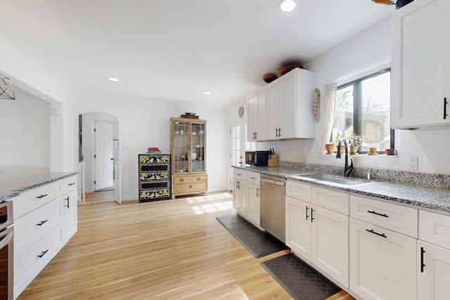 kitchen featuring arched walkways, a sink, light wood-type flooring, appliances with stainless steel finishes, and recessed lighting