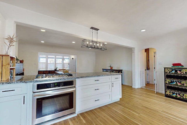 kitchen with stone countertops, light wood-type flooring, white cabinets, appliances with stainless steel finishes, and arched walkways