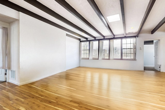 spare room featuring visible vents, beam ceiling, and wood finished floors