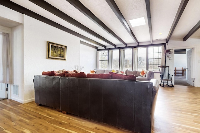 living room featuring light wood-style flooring, beamed ceiling, baseboards, and visible vents