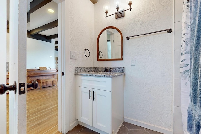 bathroom with tile patterned floors, vanity, a textured wall, and baseboards