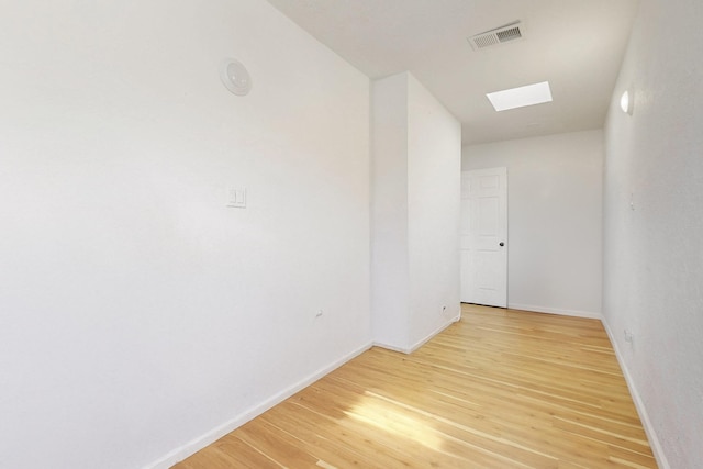 empty room featuring a skylight, baseboards, visible vents, and light wood-style floors