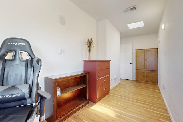 hall featuring light wood-style flooring, a skylight, baseboards, and visible vents