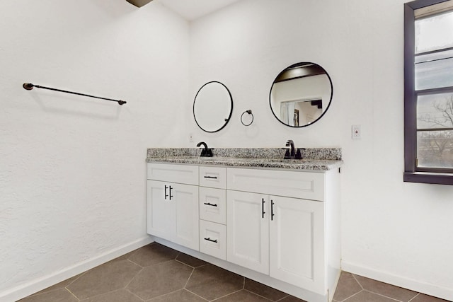 full bath featuring tile patterned floors, double vanity, baseboards, and a sink