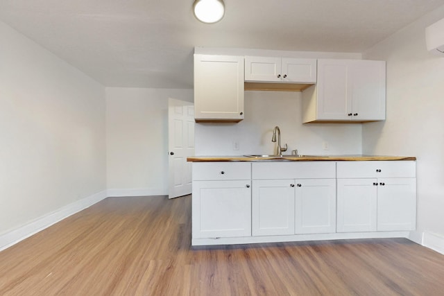 kitchen featuring white cabinets, baseboards, a sink, and wood finished floors