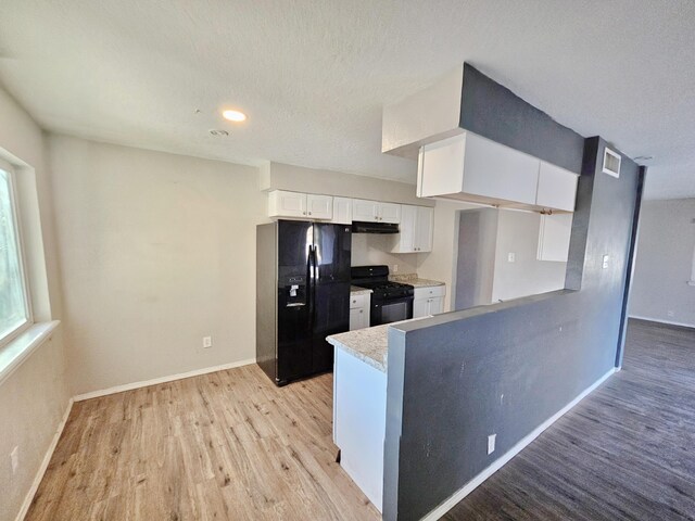 kitchen with light wood-type flooring, white cabinetry, black appliances, under cabinet range hood, and baseboards