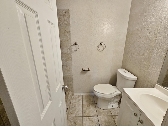bathroom featuring a textured wall, tile patterned flooring, vanity, and toilet