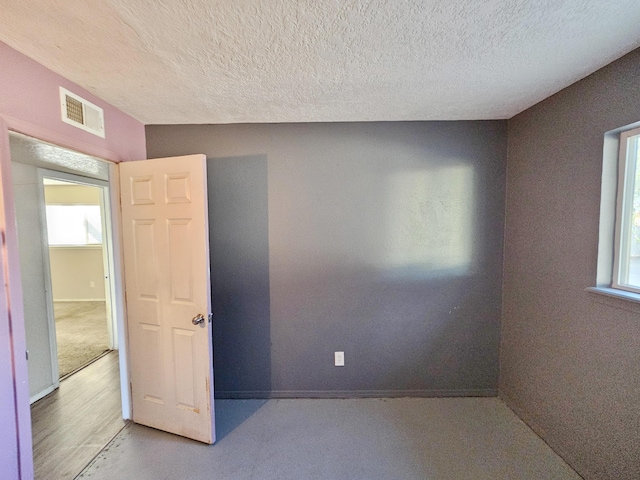 empty room with visible vents, a textured ceiling, and baseboards