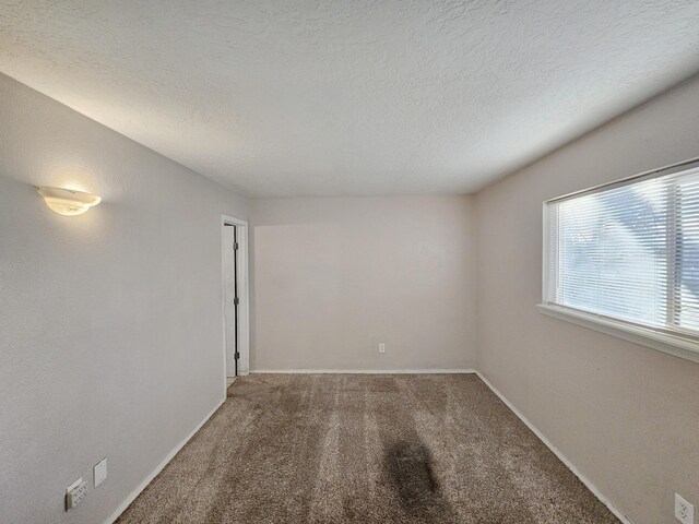 carpeted spare room featuring a textured ceiling and baseboards