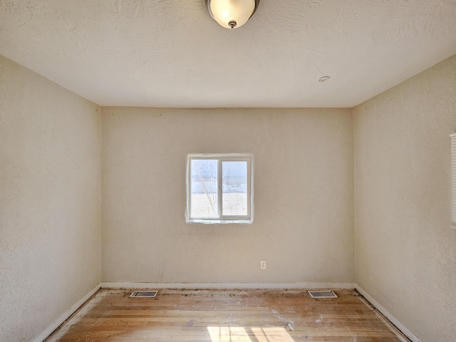 empty room featuring wood finished floors, visible vents, and baseboards