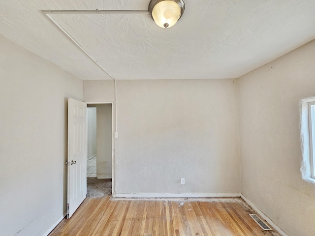 empty room featuring visible vents, light wood finished floors, and baseboards