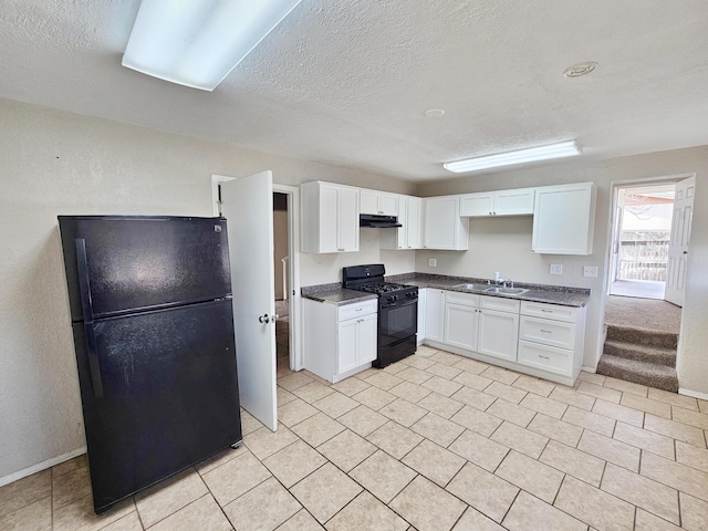 kitchen featuring white cabinets, a sink, dark countertops, under cabinet range hood, and black appliances