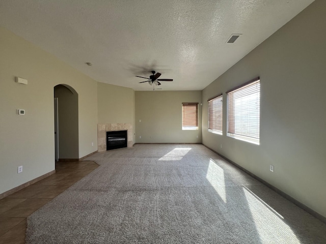 6204 Corte Alzira NW, Albuquerque, NM 87114 - unfurnished living room with ceiling fan, arched walkways, a textured ceiling, visible vents, and a tiled fireplace