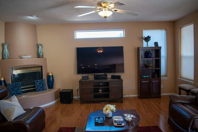 living room featuring a glass covered fireplace, wood finished floors, a textured ceiling, and ceiling fan