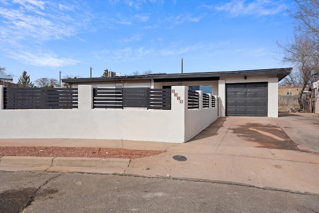 view of front facade featuring a fenced front yard, concrete driveway, an attached garage, and stucco siding